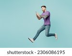 Full body side view fun young man he wears purple t-shirt jump high hold in hand use mobile cell phone run fast isolated on plain pastel light blue cyan background studio portrait. Lifestyle concept