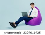 Small photo of Full body young employee IT business man corporate lawyer wears classic formal shirt tie work in office sit in bag chair hold use work on laptop pc computer isolated on plain pastel blue background