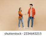 Small photo of Full body side view young smiling fun couple two friends family man woman wear casual clothes looking to each other shaking hands together isolated on pastel plain light beige color background studio