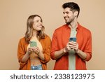 Small photo of Young happy couple two friends family man woman wear casual clothes hold in hand use mobile cell phone together look to each other isolated on pastel plain light beige color background studio portrait
