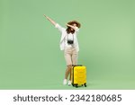 Full length traveler tourist woman in casual clothes hat hold suitcase doing dab hip hop dance gesture isolated on pastel green background. Passenger travel abroad weekends. Air flight journey concept