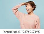 Small photo of Young excited overjoyed woman wear beige knitted sweater casual clothes hold hand at forehead look far away distance isolated on plain pastel light blue background studio portrait. Lifestyle concept