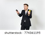 Small photo of Young sad concerned disquieted business man in black suit holding golden credit card, mobile phone isolated on white background for advertising. Concept of achievement and wealth in 25-30 years