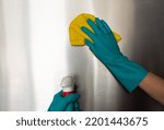 woman in blue rubber gloves dusts a switch with a microfibre cloth and uses a germ-removing spray. Cleaning concept, household introduction, clean house, no germs, covid-19