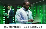 Small photo of Portrait of handsome African American young man cryptograph standing in big data storage and working as typing on laptop computer. Male Caucasian analytic on background. Information security concept.