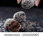 Small photo of Choco Almond Energy Balls are neatly presented, and there is a hand reaching out to take one, isolated against a slightly grayish black background.