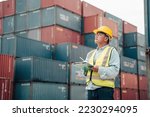 Male foreman wearing a helmet inspects the order of the container. and plan the placement of containers in a systematic transfer station full of containers.