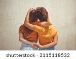 Strong female friendship. Rear view two teen girls best friends holding hands behind back and hugging while standing in front of beige wall outdoors