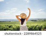 Happy young woman walks through the vineyard. White female in casual clothes and straw hats look at the landscape. Happiness and travel concept. Copy space.