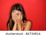Playful shy woman hiding face laughing timid. Cute Chinese Asian / Caucasian woman smiling happy through hands. Red background.