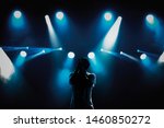 Small photo of Cool young rap singer with microphone on bright backlit stage in bright blue lights.Hip hop star performing solo set on scene in music hall.Popular rapper sings a song on rock festival in nightclub