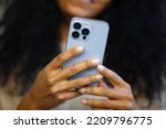 Black woman using mobile phone. African female person browsing app on modern smartphone. Download stock photo of new cellphone with triple camera