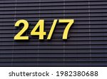 Small photo of 24 hours yellow sign open or working around the clock hanging on dark wall. Shop working 24 hours, sign on facade of building.