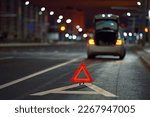 Broken down car on city street at night, red triangle - emergency stop sign behind broken blurred car. Alone damaged car at night on city highway
