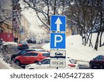 Paid parking lots in downtown, park sign on pole in winter day. Row of cars parked on snowy roadside in winter, paid parking sign. Winter parking problems. 