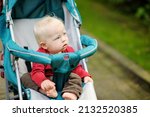 Sweet baby girl sitting in a stroller outdoors. Little child in pram. Infant kid in pushchair. Summer walks with kids. Family leisure with little child.