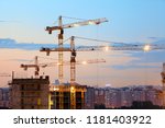 Small photo of Turret slewing cranes with lights on frame working at sundown at evening time, buildings under construction