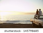 Rear view of young couple on pick-up truck parked in front of ocean enjoying sunset