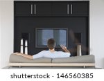 Rear view of young man using remote control while sitting on couch in living room