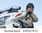 Low angle view of middle aged policeman monitoring speed through radar against sky