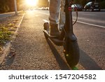 The young man is riding on the electric scooter through the evening city by the pathways