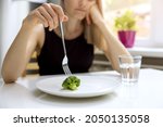 dieting problems, eating disorder - unhappy woman looking at small broccoli portion on the plate