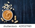 Bowl of peanut butter and peanuts on dark wooden background from top view