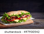 Fresh submarine sandwich with ham, cheese, bacon, tomatoes, cucumbers, lettuce and onions on wooden cutting board
