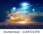 Amazing fantastic background - extraterrestrial aliens spaceship fly above clouds, ufo with blue spotlights in red glowing sky. 