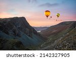 Digital composite image of hot air balloons over Epic landscape image of view down Honister Pass to Buttermere from Dale Head in Lake District during Autumn sunset