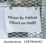 Small photo of Closeup of plain printout hung outside a small retail business in Florida: "Please Be Patient (Short on Staff)"