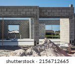 Concrete foundation and shell of a single-family house under construction, with a pile of sand for mortar mix in foreground, in a suburban development on a sunny morning in southwest Florida