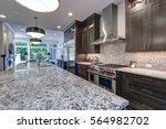 Modern kitchen with brown kitchen cabinets, oversized kitchen island, granite countertops, stainless steel hood over six burner Range and beige backsplash. Northwest, USA
