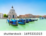 Panoramic beautiful  view of traditional venetian gondolas moored in water of Grand Canal in front of Basilica di Santa Maria della Salute church, Venice, Italy, in bight sunny day