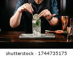 Small photo of Professional bartender pouring and preparing gin and tonic with lime at bar counter. Details of mixology