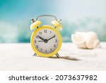 Small photo of Yellow alarm clock on summer sand sea beach with waves and seashells at background. Time for vacation travel concept. Ten o'clock