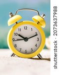 Small photo of Close up of yellow alarm clock on summer sand sea beach with waves at background. Time for vacation travel concept. Ten o'clock