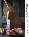 Small photo of Raw loaf of lamb with vegetables and old meat backsword over wooden table. Dark rustic style.