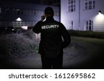 Security Guard Walking Building Perimeter With Flashlight At Night