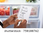 Close-up Of Young African Woman Writing Shopping List Near Open Refrigerator