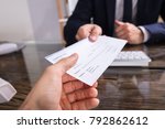 Close-up Of A Businessperson's Hand Giving Cheque To Colleague At Workplace