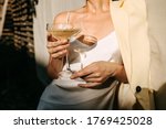 Luxurious woman wearing a white dress, holding a coupe with champagne in sun light. Concept of an open air party.