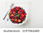 Bowl of healthy fresh berry fruit meal on white table background. Top view. Berries overhead closeup colorful assorted mix of strawberry, blueberry, raspberry, blackberry, red currant