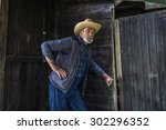 Small photo of Senior farmer or farmhand in an old rustic wooden barn standing leaning against the wall and door with a serious expression as he waits for someone