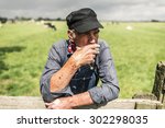 Small photo of Senior farmhand taking a smoke break leaning on the wooden fence around the pasture enjoying a cigarette