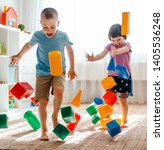 Small photo of little brother and sister run around the room spreading legs toy raznocvetnye plastikovye blocks. Children's overindulgence and clutter. Girl and boy Druzba frolic and shout, jump and have fun at home