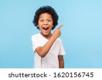 Small photo of Wow look, advertise here! Portrait of amazed cute little boy with curly hair pointing to empty place on background, surprised preschooler showing copy space for promotional ad. indoor studio shot