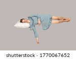 Small photo of Sleeping beauty hovering in air. Relaxed girl in vintage ruffle dress lying comfortably on pillow levitating, keeping eyes closed, watching dreams. full length studio shot isolated on gray, indoor