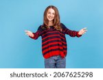 Small photo of Openhearted generous woman wearing sweater outstretching hands looking at camera with kind smile, greeting and regaling, happy glad to see you. Indoor studio shot isolated on blue background.