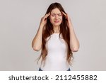 Small photo of Woman with dark hair frowning, clasping sore head, suffering intense headache, having unbearable migraine, fever and flu symptoms, wearing white T-shirt. Indoor studio shot isolated on gray background
